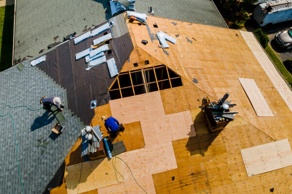Aerial view of a residential roof undergoing replacement. Several workers are installing new plywood decking and roofing materials.