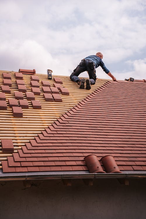 Man on a red roof working with a blue sky behind him